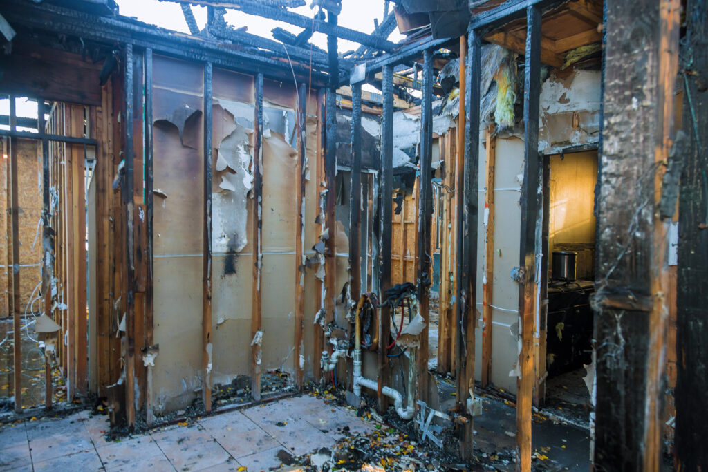 Burnt wooden walls and house with charred roof after fire